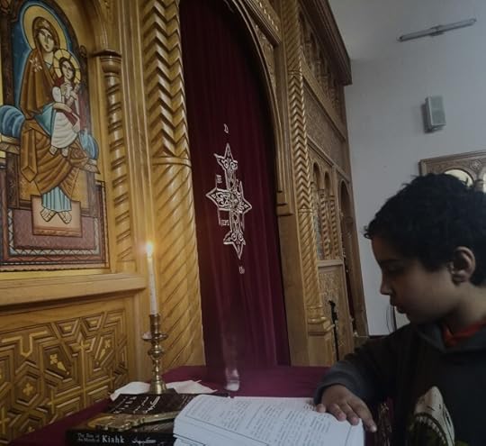 Boy praying in front of candle at church with icon of St Mary