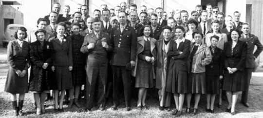 Black and white group photograph from the mid-20th century showing a large gathering of approximately 50 people, including both men and women. The group is arranged in three rows, with men predominantly in the back rows and women in the front. Most men are wearing military uniforms or suits, while women are dressed in 1940s-style dresses and coats. The central figure in the front row is a man in a military uniform with decorations, likely a high-ranking officer. The group appears to be posed outside a building, suggesting this may be a formal military or government-related event. The image captures a sense of unity and formality typical of official photographs from this era.