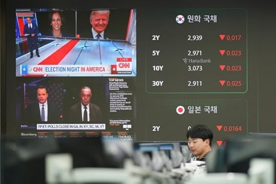 A currency trader walks by the screens showing the images of Republican presidential nominee former President Donald Trump and Democratic presidential nominee Vice President Kamala Harris