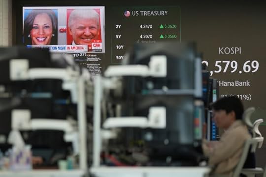 Currency traders watch their computer monitors near the screens showing the images of Republican presidential nominee former President Donald Trump and Democratic presidential nominee Vice President Kamala Harris