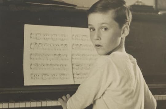 A young boy, around seven or eight years old, is seated at a piano, face turned to look at the photographer behind him.