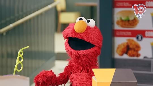 Elmo in a fried chicken store with a drink looking happy.