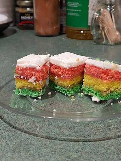 (Image of three layer cookies on a clear plate. The cookies are green, yellow and red, with a white chocolate coating.)