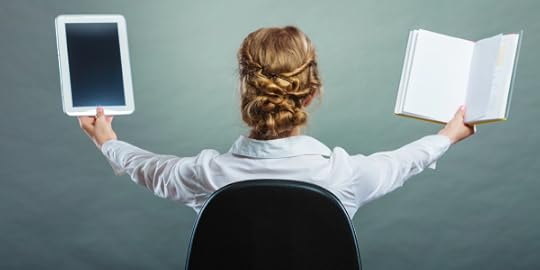 Woman from the back, holding print book in one hand and tablet in the other.
