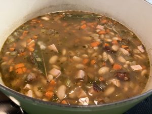 A pot of soup cooking on a stove. It's ham and bean soup with lots of vegetables.