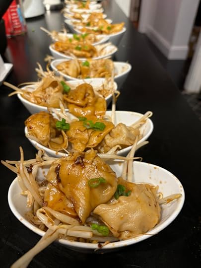 A bunch of white ceramic bowls lined up on a black countertop, each one with some beansprouts sticking out from under wontons. 