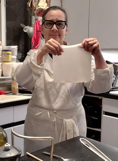 A person with black rimmed glasses holding up what looks like it could be a white washcloth or towel but is actually a sheet of noodle