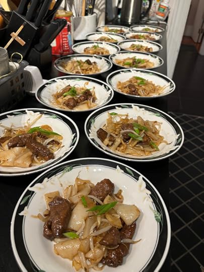 A series of black rimmed china bowls lined up on a countertop with noodles and chunks of meat in them. 