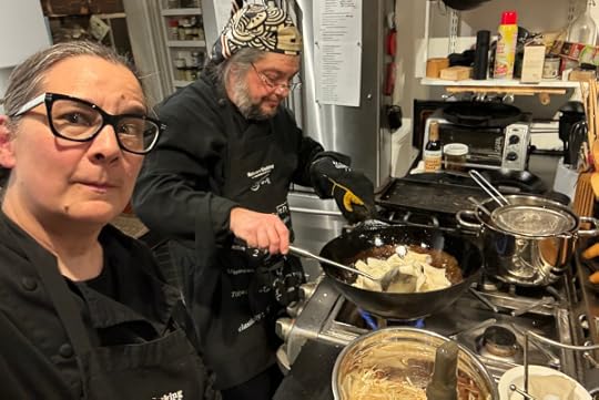 Two people in glasses and black chef jackets in front of a stove