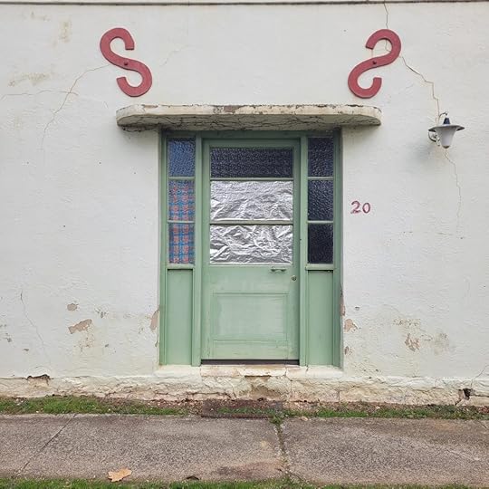 old green door in a cream wall. The door has foil in the glass. Red s-shaped metal above the doorway.