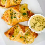 flatly of ham and cheese croissants on a white platter with dipping sauce.