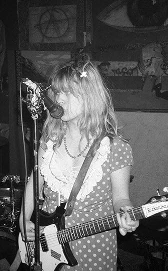 A black and white photo of Kat Bjelland of Babes in Toyland in a spotty dress playing guitar and singing into the mic