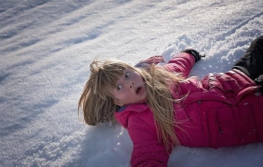Young blonde girl in pink jacket lying on snow, looking to the side, disturbed.