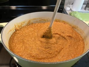 A pot of butternut squash red lentil soup that has been blended with an immersion blender. The soup is so thick that a wooden spoon is standing up in the middle of it.