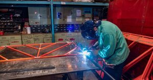 Man in a work jacket and protective face shield welding pieces of art