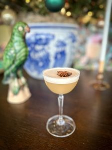 Pale yellow cocktail topped with foam and star anise in a tall stemmed glass