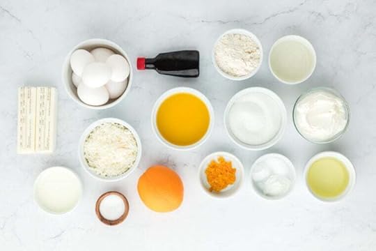 Coconut, eggs, orange juice, vanilla, and other ingredients in white bowls on white countertop
