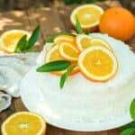 An orange coconut cake sitting on a wooden table outside before enjoying