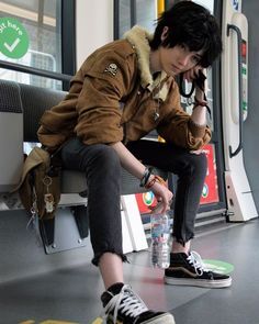 This may contain: a young man sitting on a subway bench with his hand in his mouth and holding a water bottle