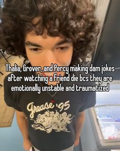 This may contain: a young man with curly hair standing in front of a computer screen and looking at the camera