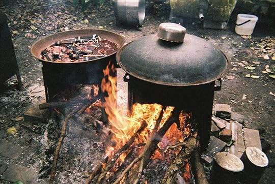 A film photo showing a bonfire heating up a closed pot while clothes are dyed in another