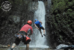 guide helping someone rappel down a large waterfall