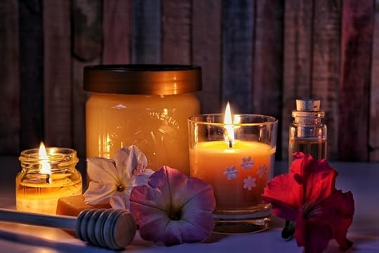 Honey jar with two votive beeswax candles and a vial of oil, and some flowers