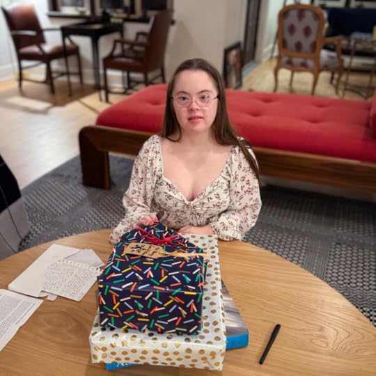 Penny sits at a wooden table with neatly wrapped presents in colorful wrapping paper in front of her.