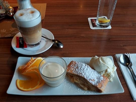 Warm apple strudel with vanilla ice cream, vanilla sauce and slices of orange and a latte macchiato.
