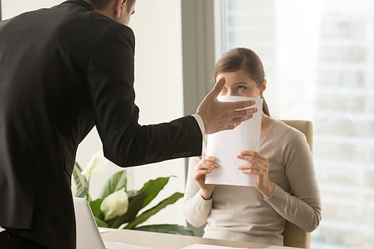 Woman covering her face with a paper while her boss leans over her desk in an intimidating way