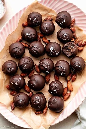 healthy date almond truffles coated in chocolate and sea salt placed with almonds on a pink plate.