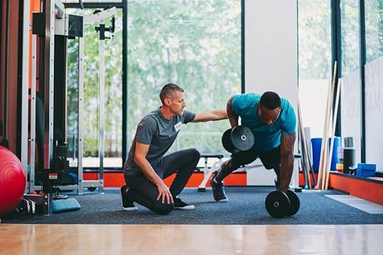 A personal trainer working in a access gym coaches his personal training client to perform dumbbell renegade rows.