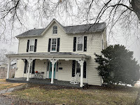 Old white clapboard home with bare trees and misty backgroun.d.