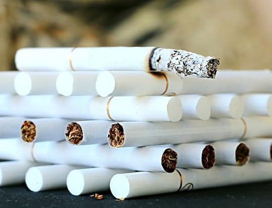 Cigarettes stacked in layers, alternating direction, with ash coming off one on top.