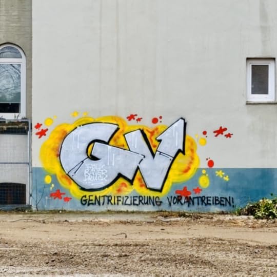 Ein großes Graffiti an einer Mauer hinter einer Brachfläche: 