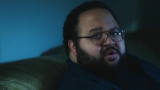 Dylan with his glasses sits on the couch at night on Severance