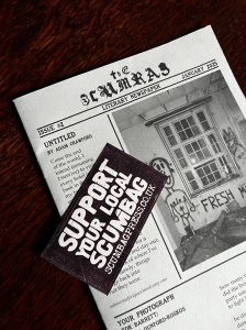 Image shows a copy of 'The Scumrag Issue 2' a newspaper style zine, with a 'support your local scumbag' sticker resting on top of it