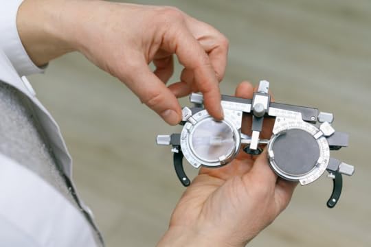 Image: an opthalmologist holds a diagnostic device shaped like a pair of eyeglasses outfitted with adjustable lenses.