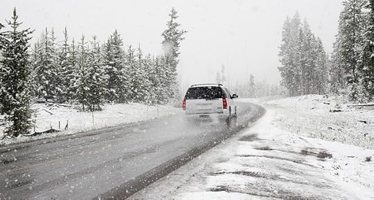 SUV driving away from camera on a snowy road with evergreen trees on either side.