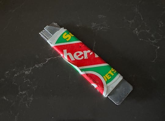 A flat metal handle with a razor blade peeking from one end, wrapped in Fisher-Price stickers
