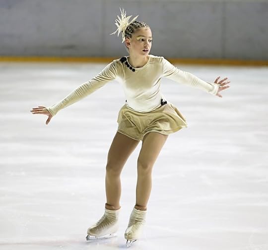 Young blonde figure skater in a beige and white costume, preparing to go into a turn.