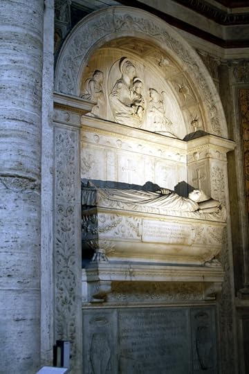 Marble tomb. The dead Cristoforo is shown lying down as if in sleep, full body and life size, on top of a grand sarcophagus. Above and behind him is an elaborate marble arch with classical decorations, and saints are pictured above him in relief. The della Rovere crest of an oak tree is visible in several places.
