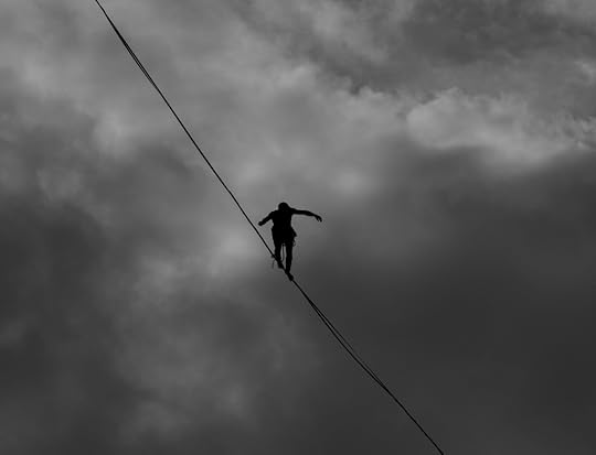 Silhouette of someone walking across a high wire, with a cloudy, overcast sky in the background.