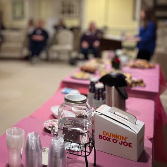 A table covered with a pink tablecloth holds an assortment of refreshments, including pastries and flowers.