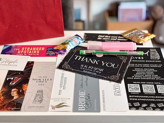 A flatlay of several author themed bookmarks and flyers, with snacks and pens ontop.