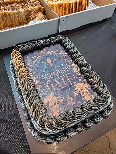 A rectangular cake with black icing, around the cover of SK Stapar's Midnight Gate.