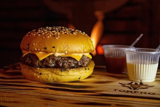 Juciy cheeseburger on thick bun sitting on a wooden wable with two dishes of sauce (one red, one white) beside it.
