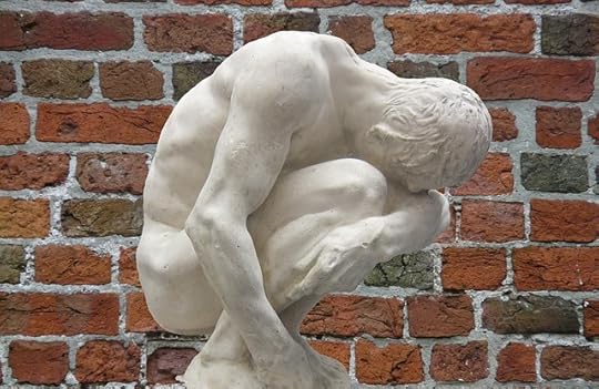 white marble statue of a man curlced around his knees in front of a red brick wall.