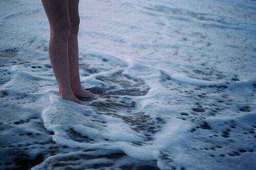 This may contain: a person standing on top of a sandy beach next to the ocean with waves coming in