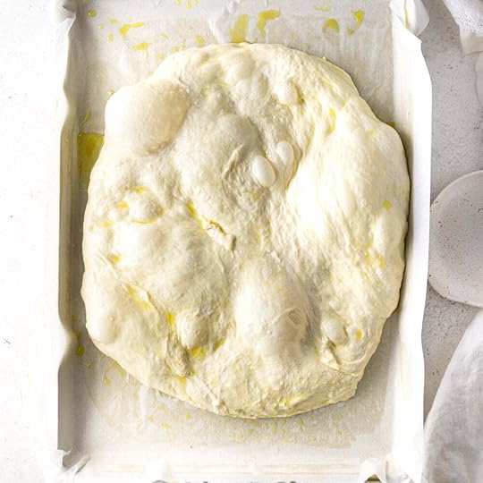 Bubbly focaccia dough in a parchnment lined baking sheet.